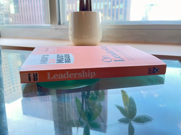 An orange book, On Leadership, sits on a glass table.